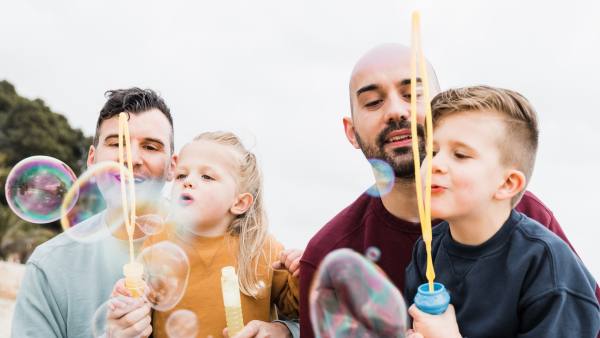 two dads blowing bubbles outside with their son and daughter