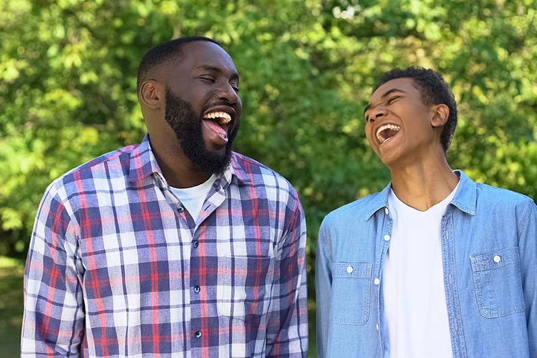 Father and son exchanghing jokes and laughing together surrounded by green foliage outdoors