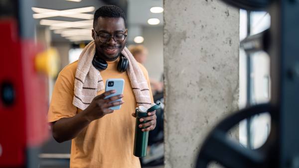 man in gym with towel, water bottle, cellphone, and headphones